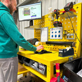 A man using a yellow multi-tiered packing bench with a workstation setup, including a computer monitor, in a warehouse environment.